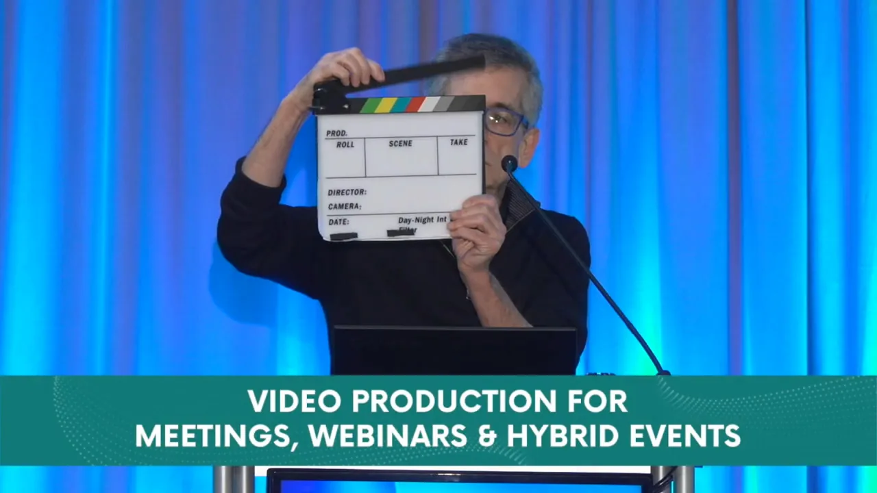 David Mayer holding a film clapperboard on stage at a corporate event production in Michigan